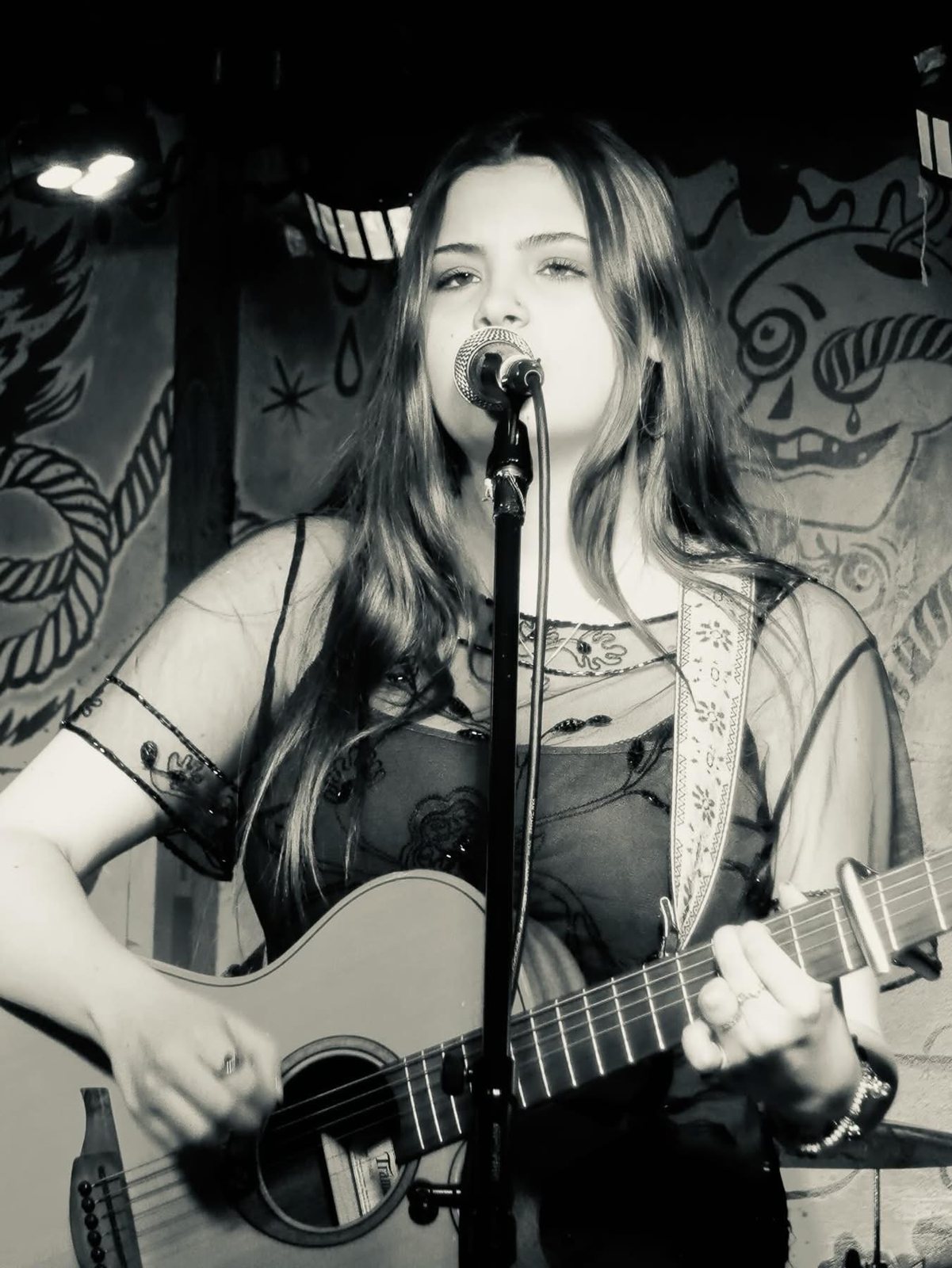 Brooke Dawn singing and playing acoustic guitar on stage, black and white